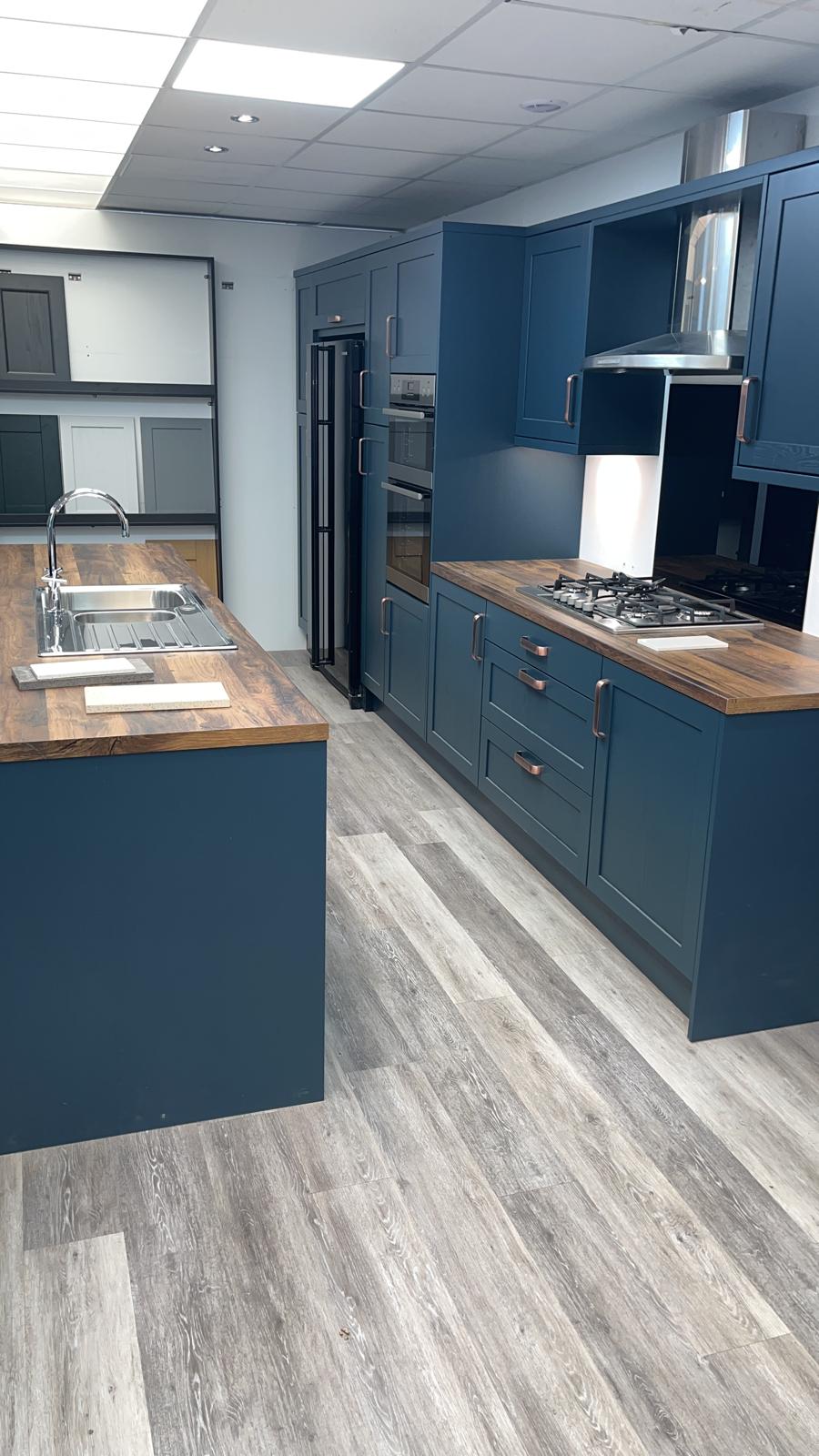A navy kitchen with wood-effect worktops and an island, seen down its length