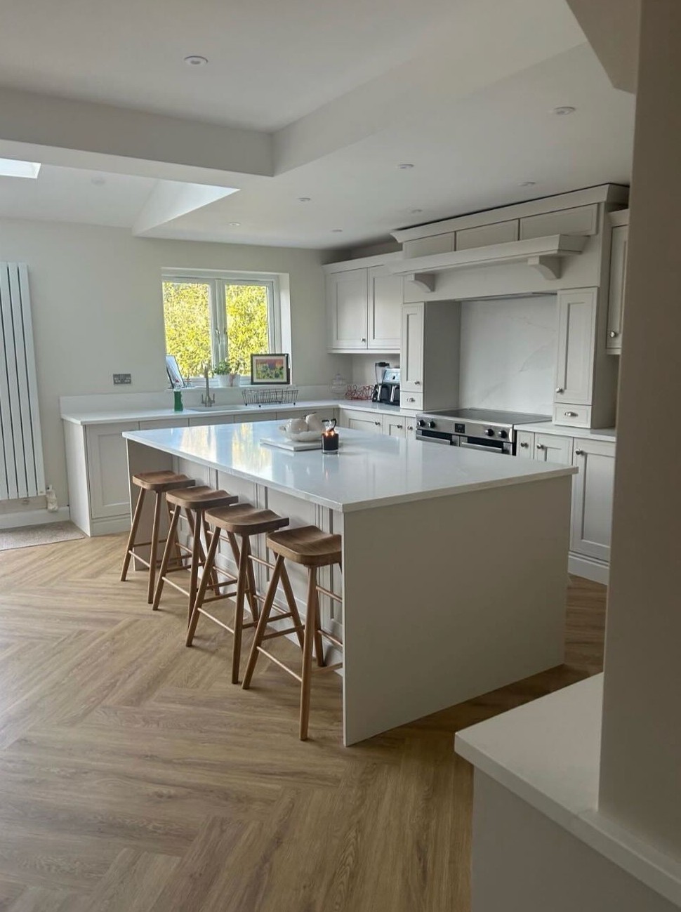 A cream kitchen with a large island, four wooden stools and a herringbone floor
